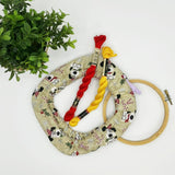 Embroidery hoop with fabric, thread, and a plant on a white background