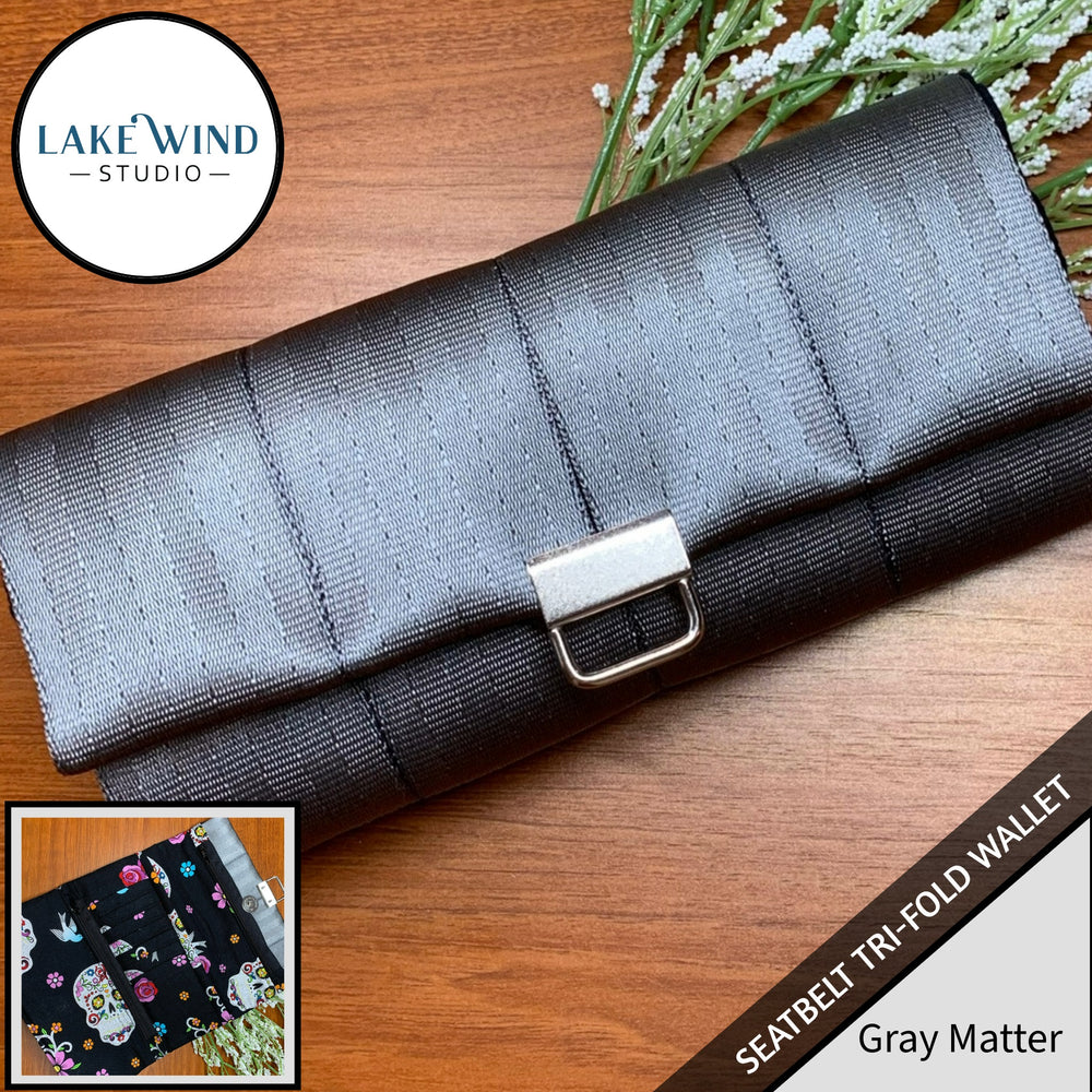 Gray tri-fold wallet with a buckle on a wooden surface, featuring Lake Wind Studio branding.