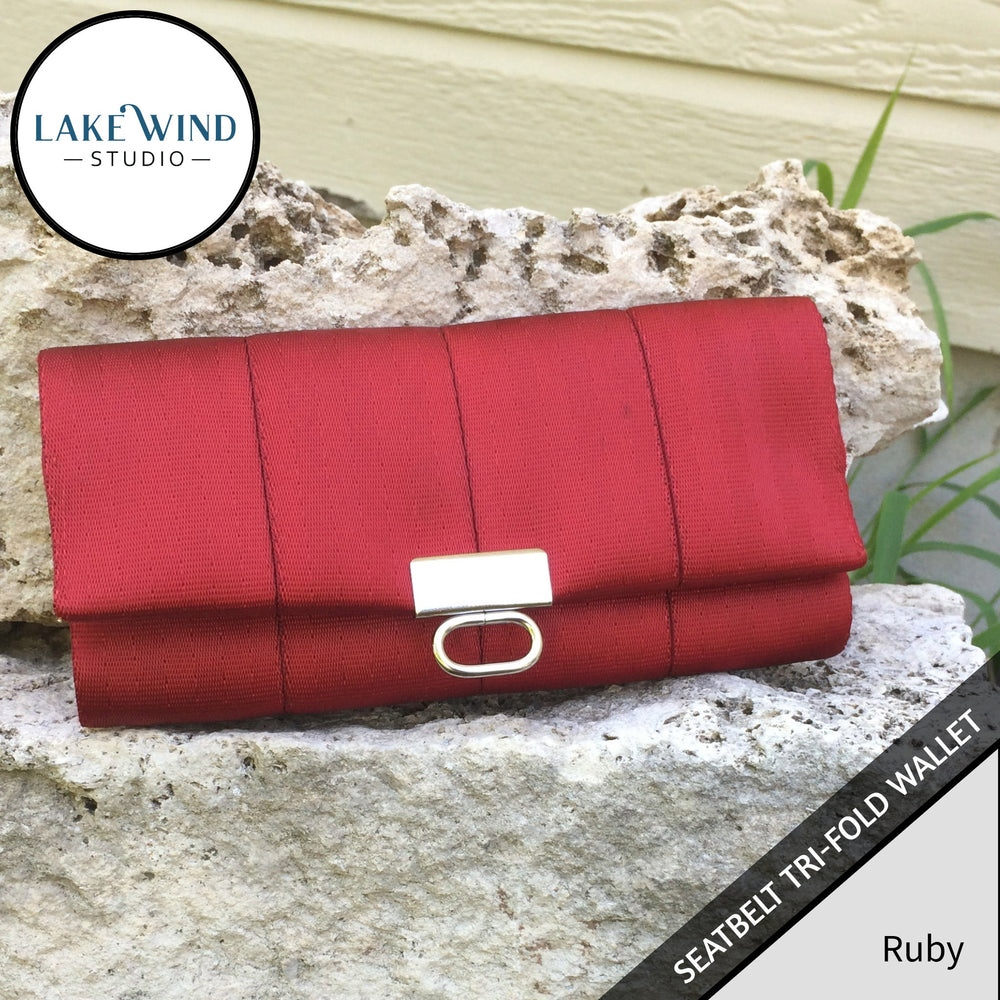Red tri-fold wallet with silver clasp on a stone surface, Lake Wind Studio branding visible.