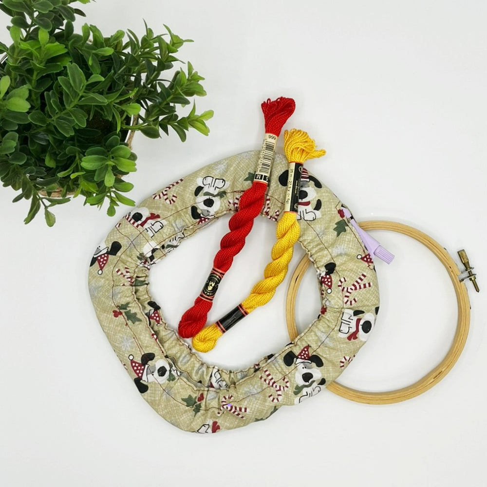 Embroidery hoop with fabric, thread, and a plant on a white background