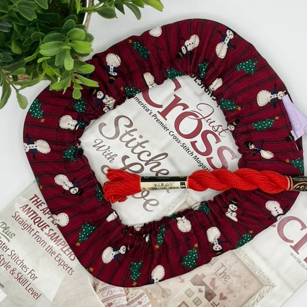 Cross-stitch grime guard for nurge frame in a snowman fabric with red background.