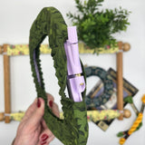 Green fabric headband with a purple pen inside, held against a decorative background.